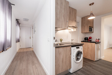 Corridor of a house with several doors and access to different rooms, open kitchen with oak furniture with white appliances