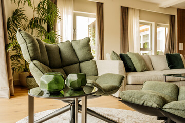 Individual green fabric sofa with footrest and round circular glass side table and decorative glass accessories