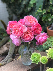 Bouquet of pink roses in a glass vase in a garden surrounded by flowers and plants