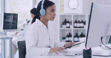 Scientist using computer, digital tablet, listening to music on headphones and working in laboratory. Focused pathologist or biochemical engineer using technology and binaural beats for concentration