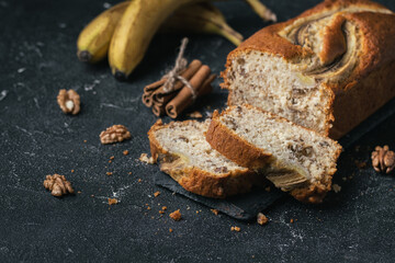 Fresh banana pie cut pieces on a black concrete background next to bananas and walnuts. Homemade pastry concept.