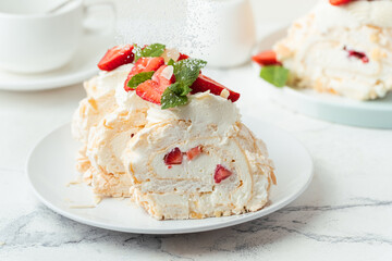 Meringue roll sprinkled with powdered sugar decorated with strawberries sliced and served in the white plate on the white background. Macro shot