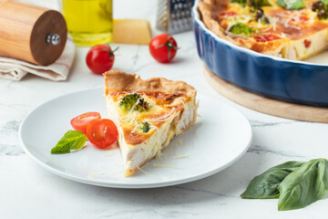 Quiche with chicken decorated with tomatoes, basil and broccoli. French pie with shortcrust pastry base on the white marble background