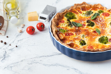 Quiche with chicken decorated with tomatoes, basil and broccoli. French pie with shortcrust pastry base on the white marble background