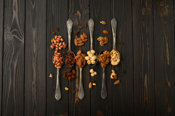Hazelnut, cashews, raisins, almonds, peanuts, walnuts in silver spoons on a rustic background