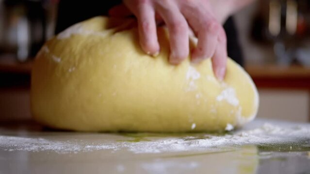 Female Hands Kneading Yeast Dough on the Kitchen Table Sprinkled with Flour. Loose, yellow, smooth dough for making bread, buns. Cooking sweet delicious pastries for the family. Slow-motion. Close-up.