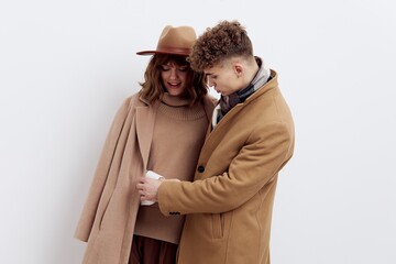 a sweet, beautiful, loving couple stands on a white background in stylish autumn clothes, gently cuddling up to each other and a man looks at a woman in a hat