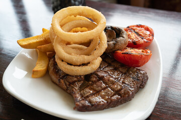 Shallow focus on battered onion rings on a plate with a steak and chips with tomatoes and mushrooms. - 515928602
