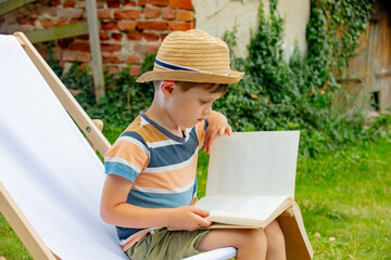 Funny little boy with a book sits in chair in outdoor