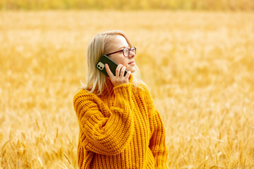 girl in eyeglasses and yellow sweater with mobile phone in wheat field