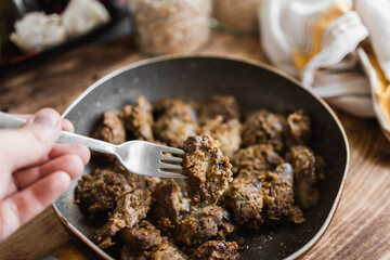homemade fried liver on a fork held in your hand in the kitchen (selective focus, blurred background)