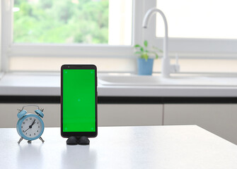 Smartphone with a green blank screen on the kitchen table against the background of the window.