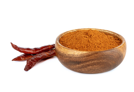 Wooden bowl with ground red pepper and hot pepper pods on a white background.