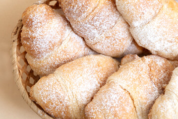 Homemade butter croissants sprinkled with powdered sugar on wicker tray