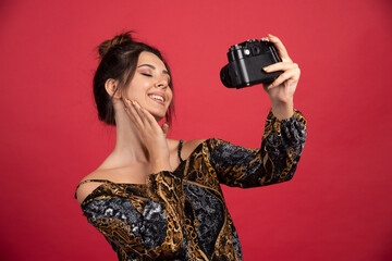 Brunette girl holding a professional dslr camera and takes her cheerful selfies