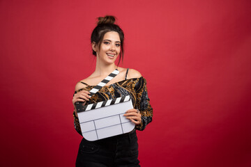 Brunette girl holding a blank clapper board for film production on red background