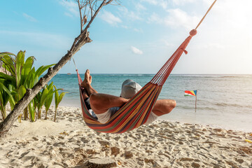 Tourist relaxing in a hammock on a tropical beach overlooking the Indian Ocean. La Digue island,...