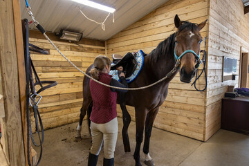 Woman putting a saddle on her horse in a stall