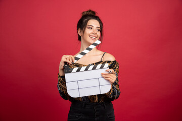 Brunette girl holding a blank clapper board for film production on red background