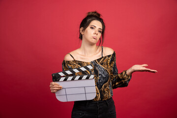 Brunette girl holding a blank clapper board and thinking about what to do with it