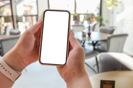 Mockup image of woman's hands holding white mobile phone with blank screen in cafe