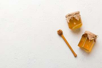 Glass jar of honey with wooden drizzler on colored background. Honey pot and dipper high above. Top...