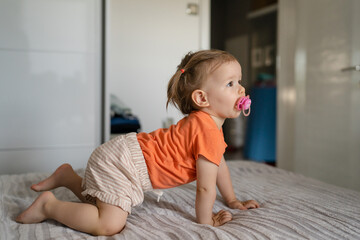 One caucasian girl with nipple pacifier crawling on the bed at home toddler or baby domestic life...