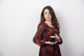 Wavy haired woman with cup of tea standing on gray background