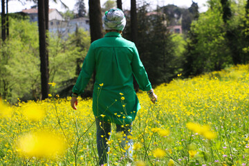 Yellow buttercup growing in forests and mountains in spring. The wonderful-looking buttercup is actually a type of poisonous flower. Arab woman in green dress walking in yellow flowers	
