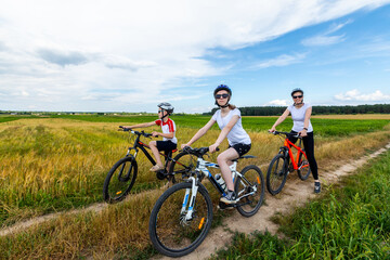 Naklejka premium happy family on bike ride outdoors. Happy mother and kids on bikes cycling outdoors. active family sport and fitness together