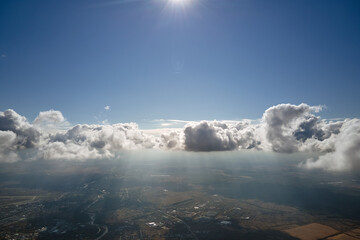Aerial view from airplane window at high altitude of distant city covered with white puffy cumulus...