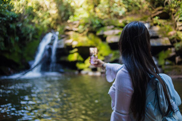 Mujer tomando una foto con su celular a una cascada en la selva. Concepto de viajes y turismo