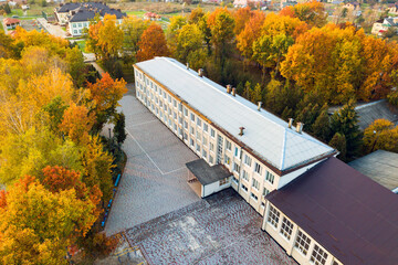 Aerial view of school, college or kindergarten building with big yard among autumn trees on rural landscape background