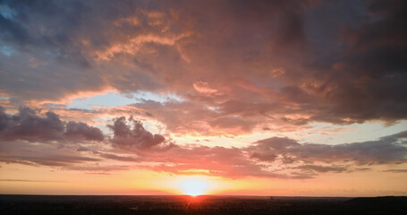 Obraz premium Bright colorful sunset sky with setting sun and vibrant clouds over dark landscape