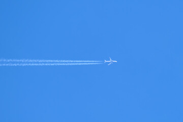 Distant passenger jet plane flying on high altitude on clear blue sky leaving white smoke trace of contrail behind. Air transportation concept