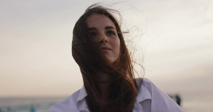 Young woman amazedly looking on the overcast windy sky, slow motion wind blowing hair