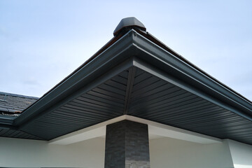 House corner with brown metal planks siding and roof with steel gutter rain system. Roofing,...