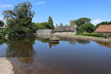 Fototapeta na wymiar The hexagonal duck house on the village pond at East Quantoxhead in Somerset, England. Thatched cottages can be seen in the background
