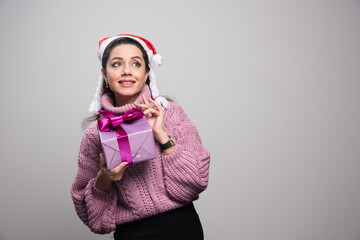 Christmas portrait of smiling Santa woman holding gift box on gray background.