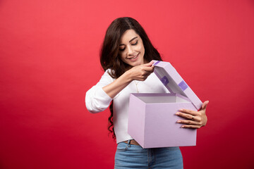 Young woman holding an opened present on a red background