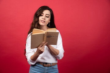 Young woman reading a book on a red background