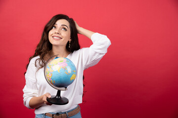 Young woman posing with globe on red background