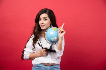 Happy woman posing with globe and magnifying glass while pointing up