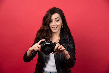 Beautiful woman photographer looking on a photo camera on a red background