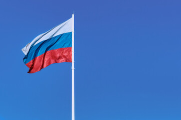 Waving Russian flag against a blue sky and empty space for text. Room for text. National flag of the Russian Federation. Silky shiny texture.