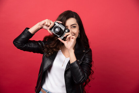 Woman photographer taking pictures with a photo camera on a red background
