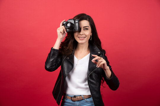 Woman photographer taking pictures with a photo camera on a red background