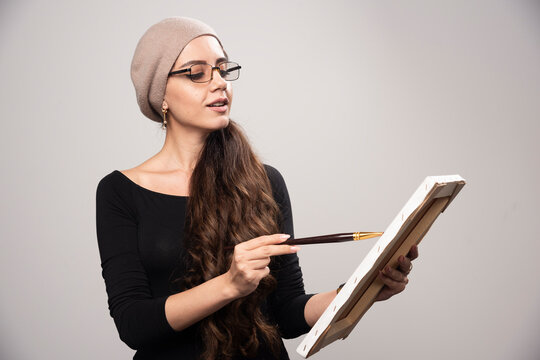 Young artist girl showing her artwork to the public and explaining details with the halp of brush