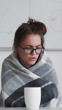Vertical video. Sick business woman. Online meeting. Remote conference. Unwell female office worker in blanket with flu sneezing feeling cold working from home drinking tea.