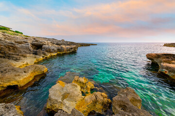 The rocky coast and turquoise Mediterranean Sea at the coastal town of Binibeca Vell at sunset on the Balearic island of Menorca, Spain.